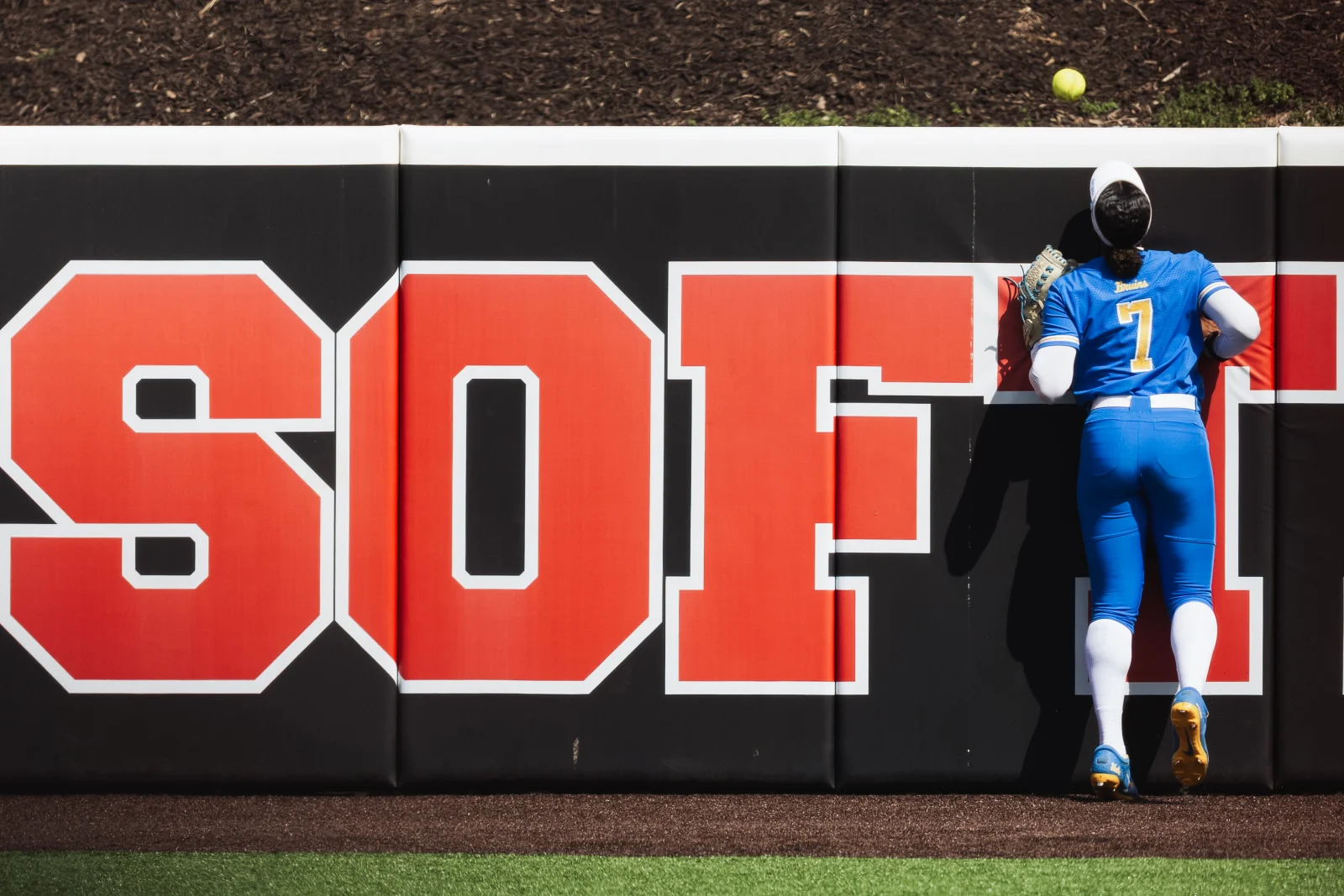 UCLA outfielder Jolyna Lamar (7) looks up helplessly as a home run by Nebraska's Hannah Camenzind clears the wall during the Cornhuskers' six-run second inning at Bowlin Stadium in Lincoln, Neb., Sunday, March 29, 2026. The outfield padding behind her spells out "SOFT." Nebraska won 8-4 to clinch the series.